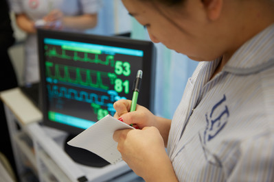 Student nurse taking notes next to monitor screen